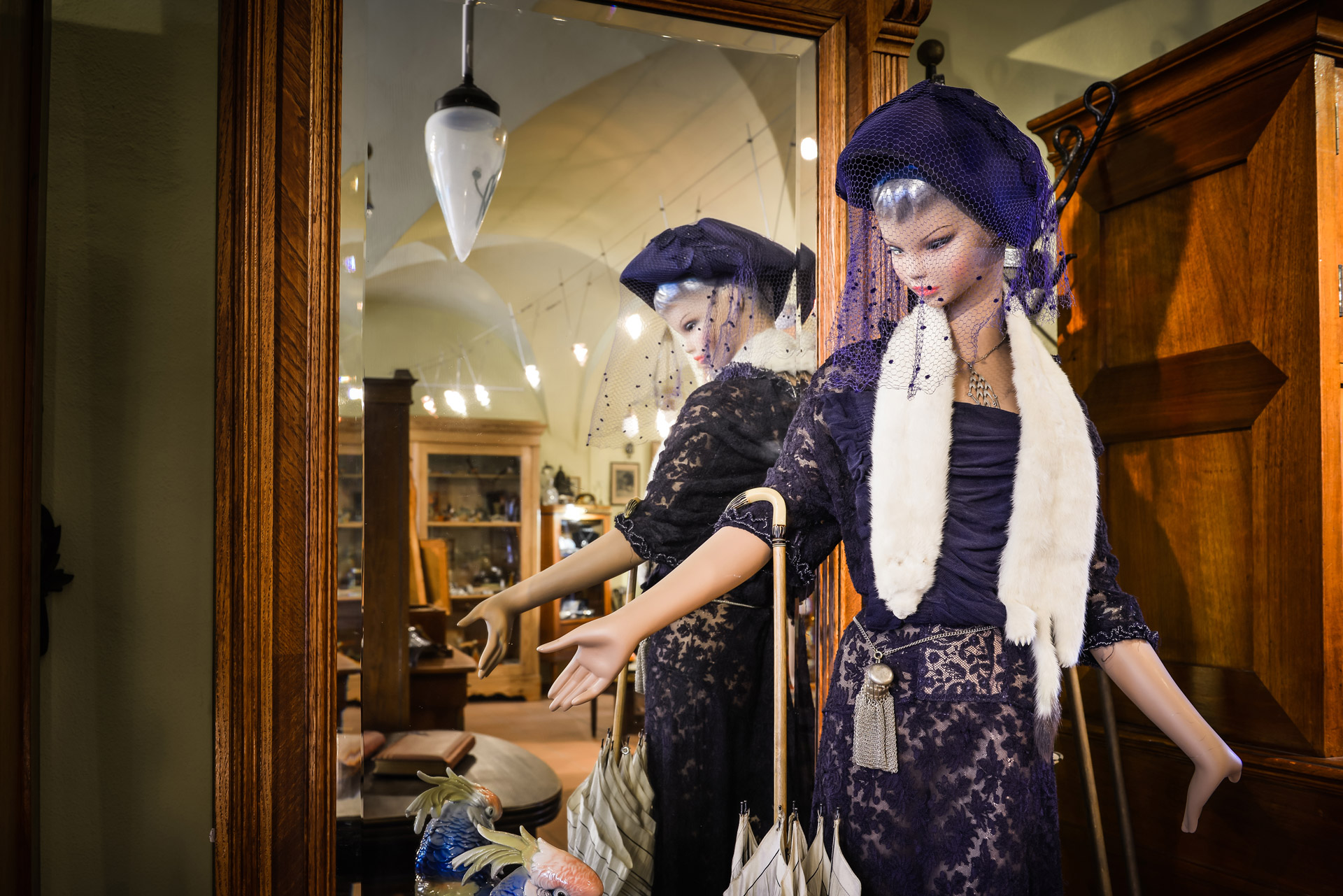 Schaufensterpuppe im violetten Kleid mit Hut vor einem hölzernen Spiegelschrank